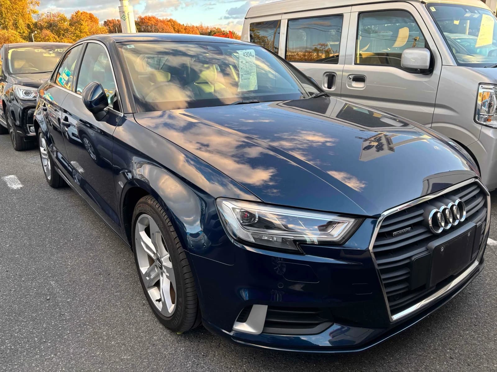 Front three-quarter view of a dark blue Audi A3 quattro sedan parked in an outdoor lot with autumn trees in the background