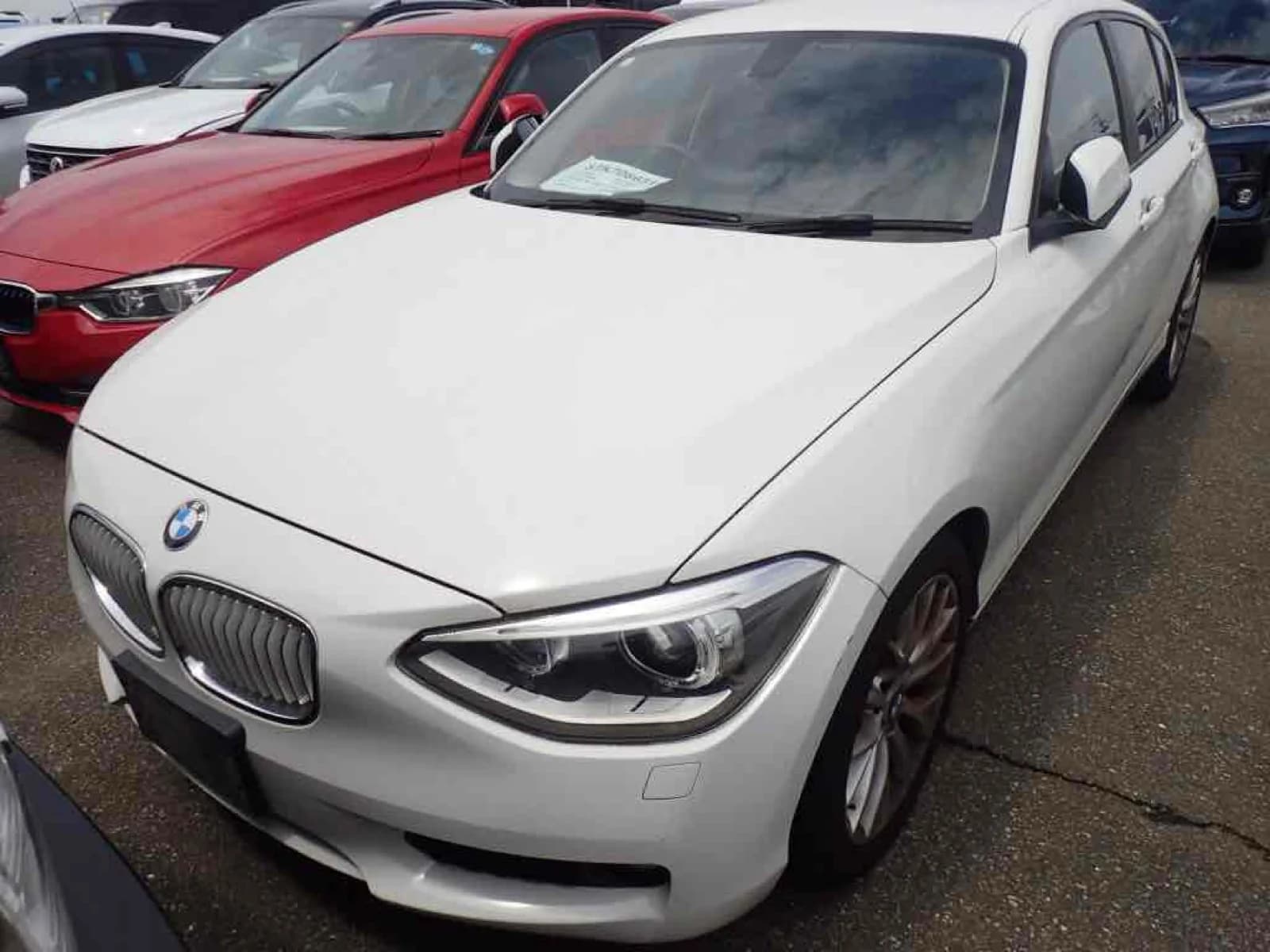 Front three-quarter view of a white BMW 1 Series hatchback parked among other cars in an outdoor lot