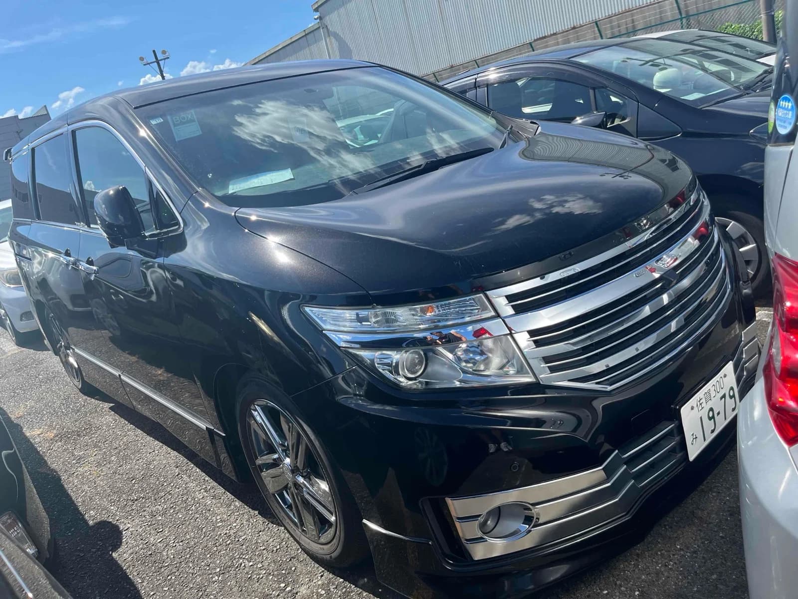 Black Nissan Elgrand Rider Autech minivan, front three-quarter view showing chrome grille, headlights, and Rider badge, parked among other cars