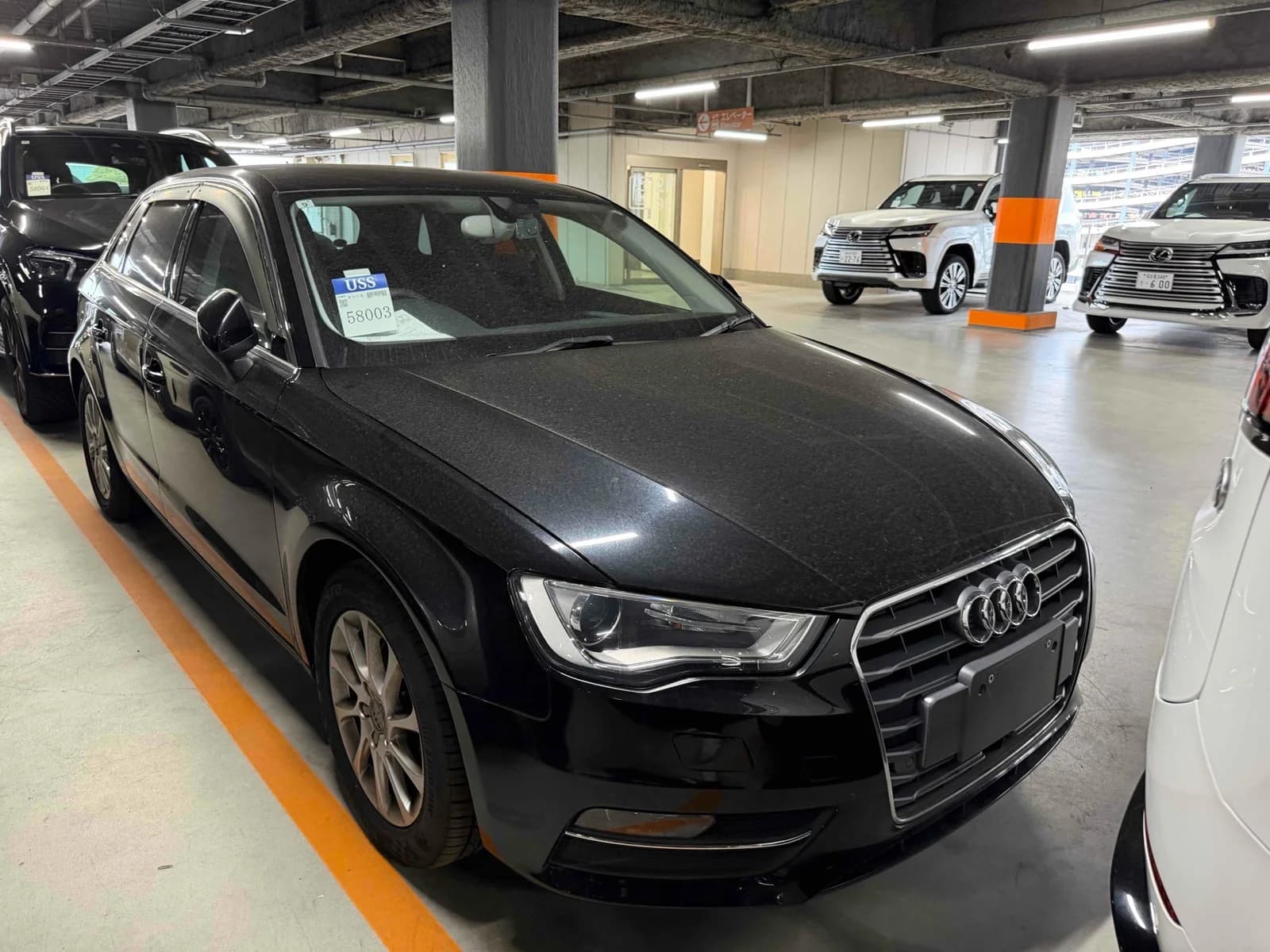 Front three-quarter view of a black Audi A3 sedan inside an auction inspection garage