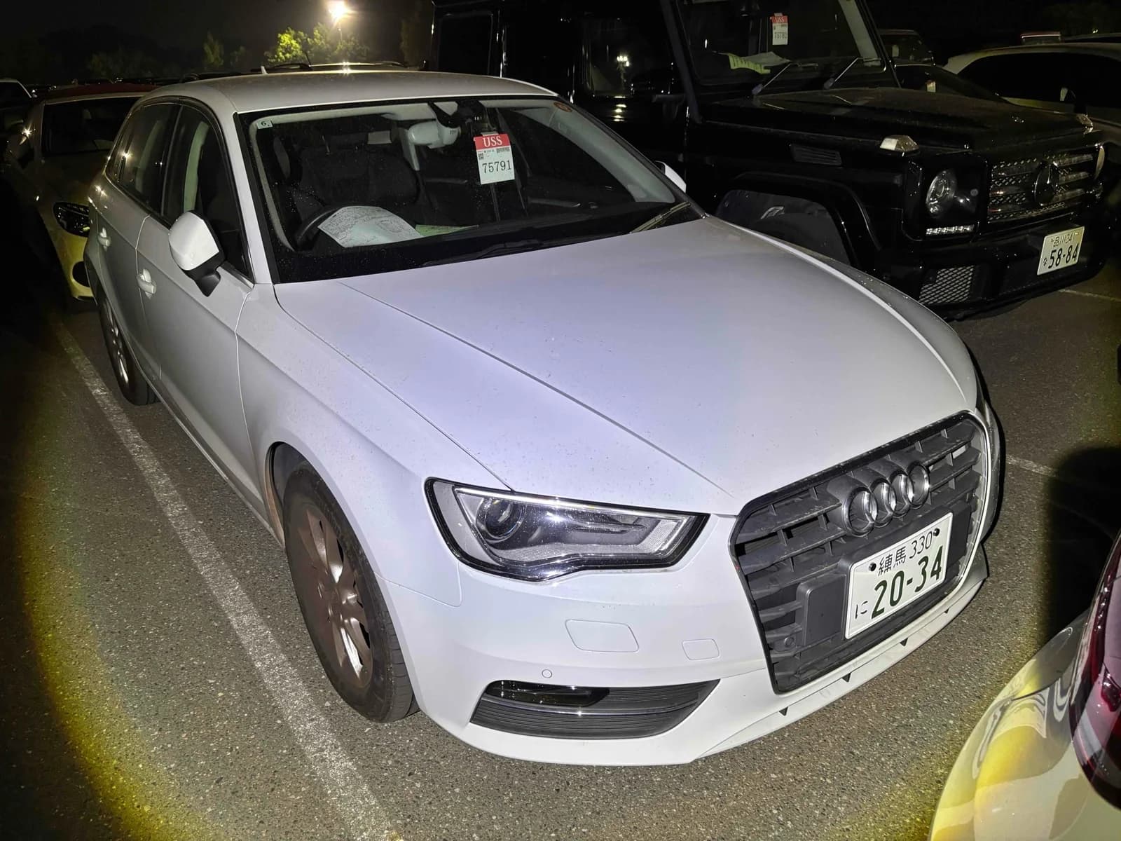 Front three-quarter view of a white Audi A3 sedan parked at night in an outdoor lot