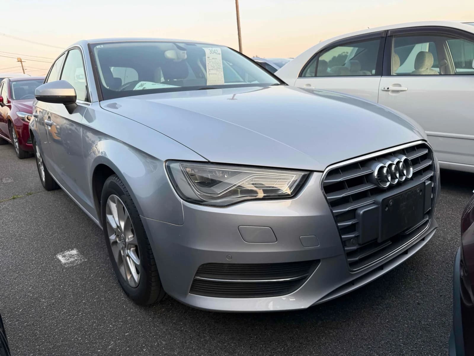 Front three-quarter view of a silver Audi A3 sedan parked in an outdoor auction lot at sunset