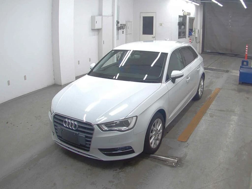 Front three-quarter view of a white Audi A3 Sportback inside an auction inspection bay