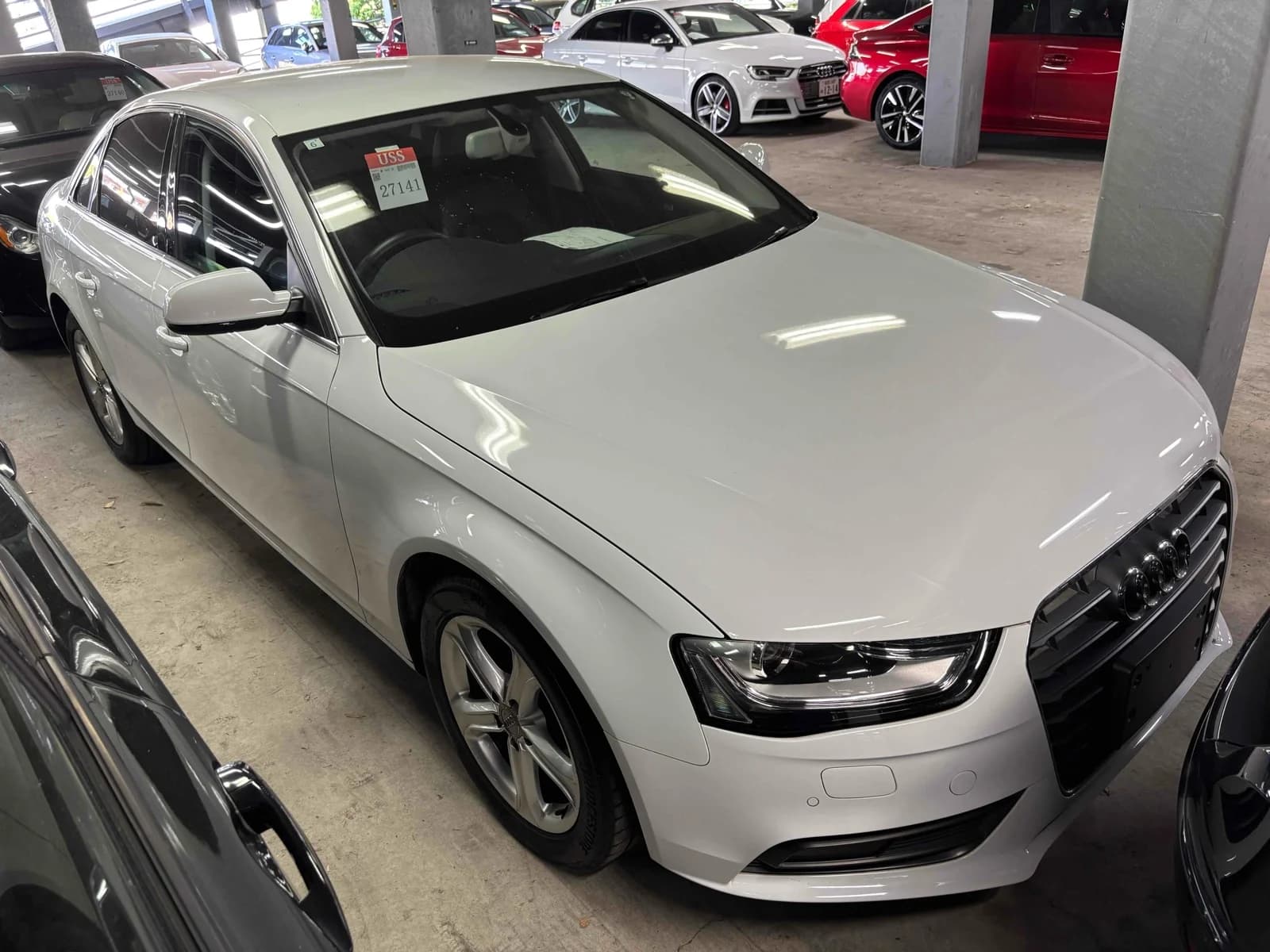 Front three-quarter view of a white Audi A4 sedan parked in a multi-level auction lot