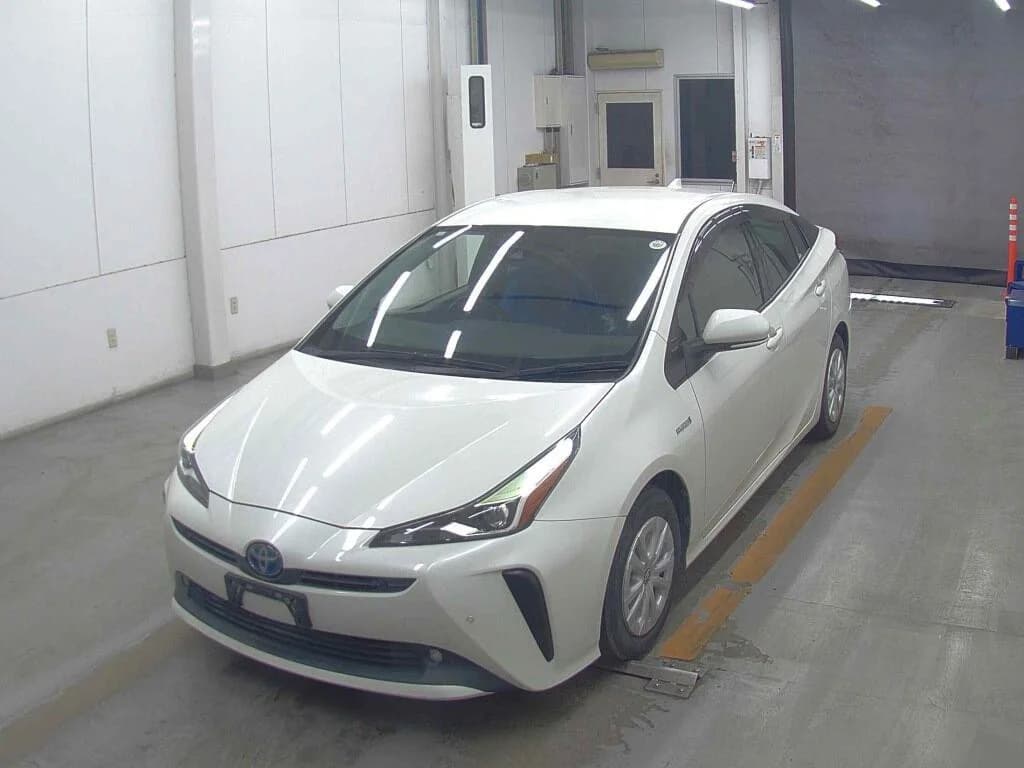 2020 Toyota Prius S hybrid in pearl white - front-left 3/4 view with LED headlights, blue hybrid Toyota emblem, and silver wheel covers in an auction inspection bay