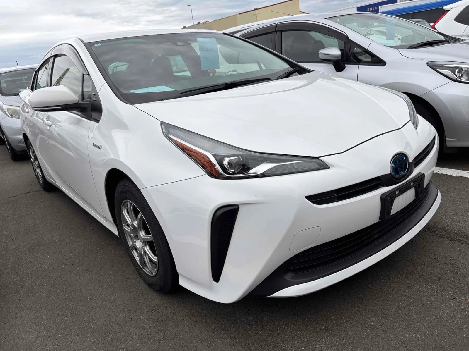 2019 Toyota Prius E hybrid in pearl white - front-right 3/4 view with LED headlights, blue hybrid Toyota emblem, window visors, and aftermarket alloy wheels