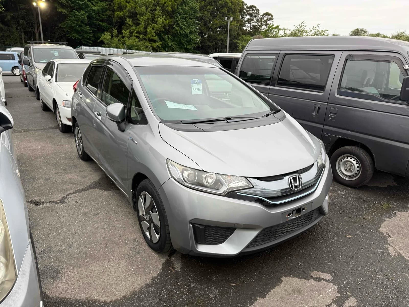 Silver Honda Fit Hybrid, front three-quarter view showing the Honda badge and chrome grille, parked in an outdoor auction lot
