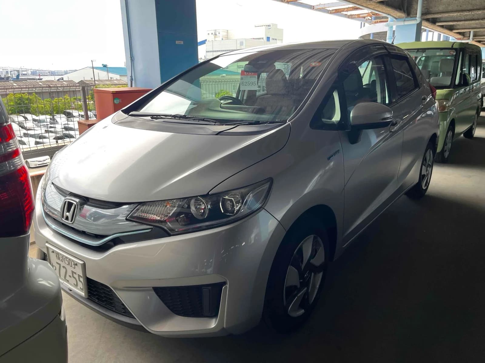 Silver Honda Fit Hybrid, front three-quarter view showing the Honda badge and chrome grille, parked in a covered multi-storey auction lot
