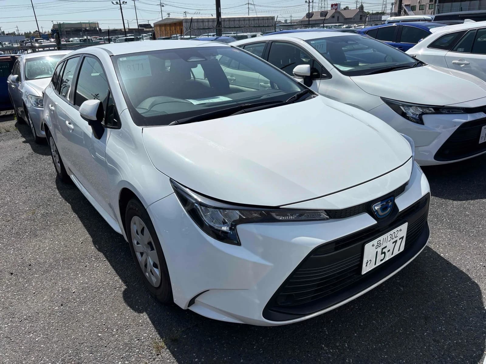 Toyota Corolla hybrid hatchback - Front-left 3/4 exterior view showing white pearl paint, LED headlights, and dark alloy wheels at parking lot