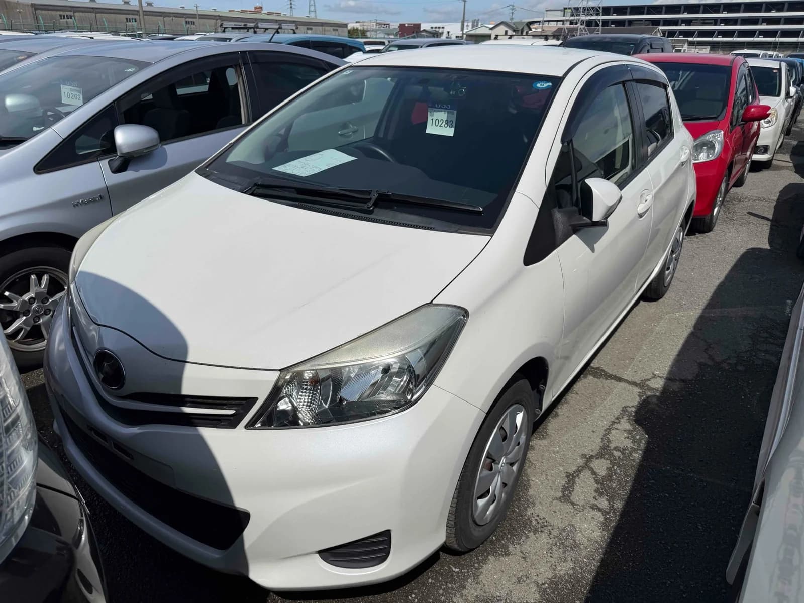White Toyota Vitz hatchback, front three-quarter view showing headlights, grille, and Toyota badge, parked in an outdoor auction lot