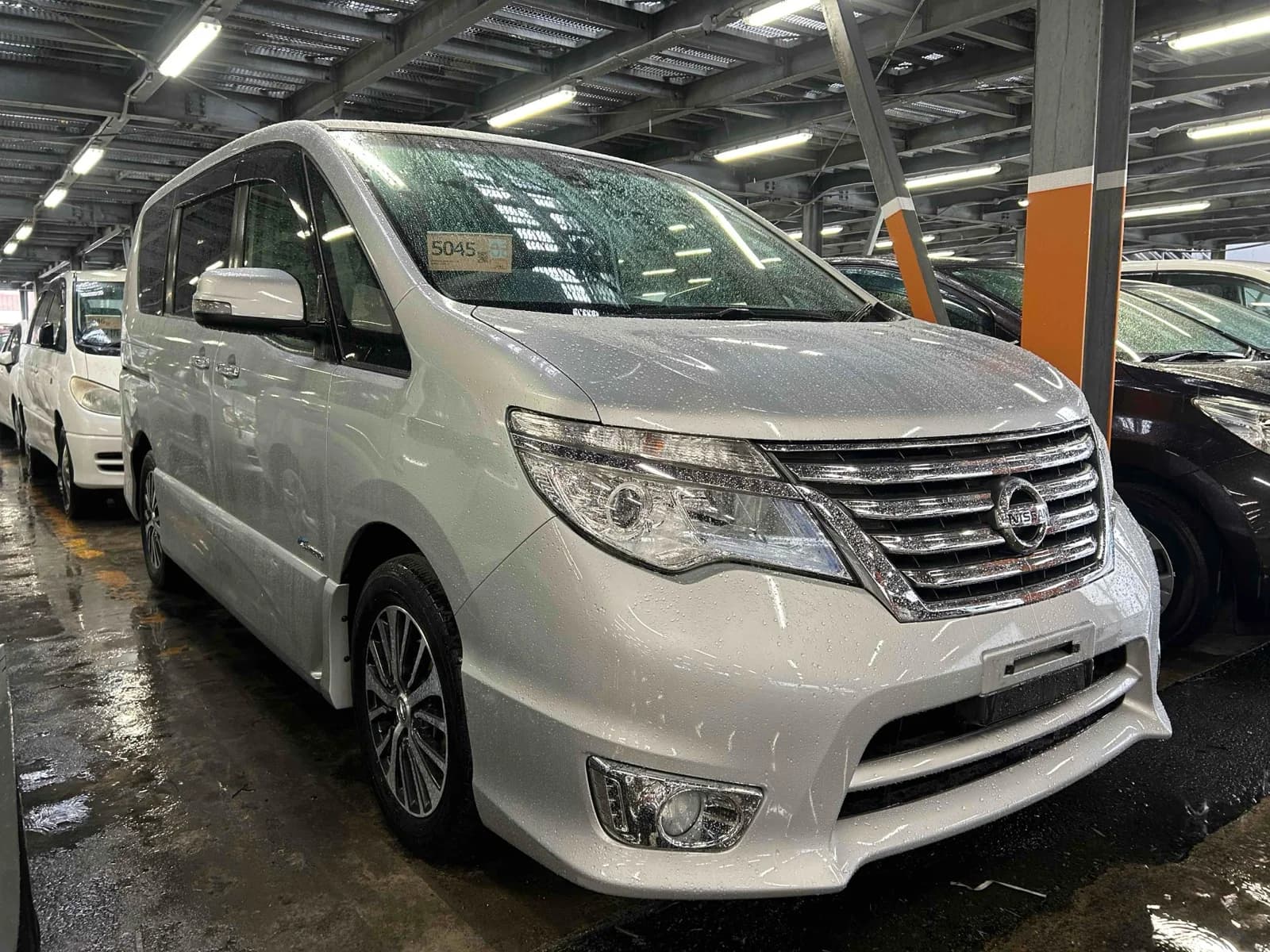 Pearl white Nissan Serena Highway Star minivan, front three-quarter view showing chrome grille and headlights, parked in a covered auction inspection area