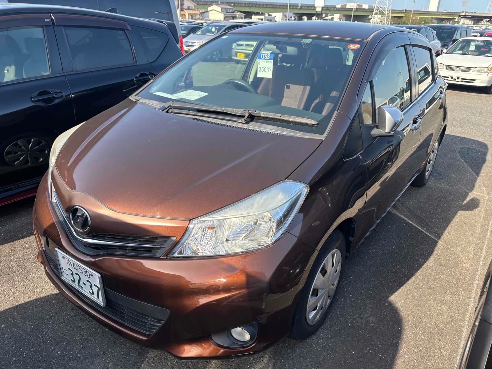 Bronze Toyota Vitz hatchback, front three-quarter view showing headlights, grille, and Toyota badge, parked in an auction lot