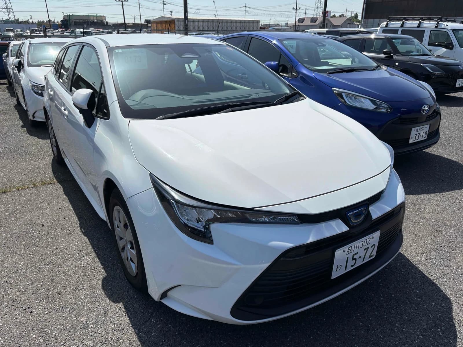 Toyota Corolla hybrid hatchback - Front-left 3/4 exterior view showing white pearl paint, modern LED headlights, and dark alloy wheels in parking lot