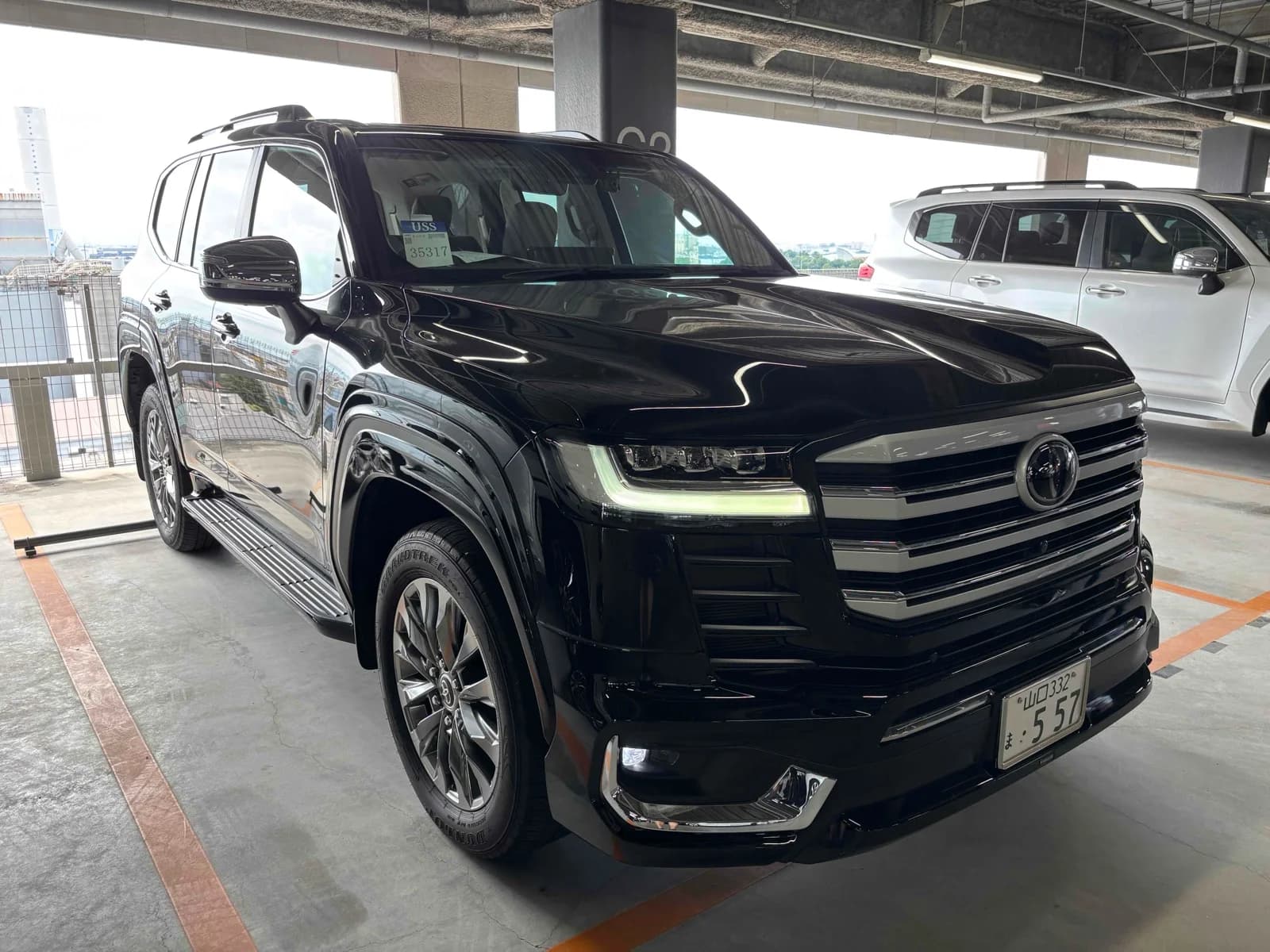 Black Toyota Land Cruiser 300 Series luxury SUV front-left three-quarter view at covered auction warehouse with LED headlights and chrome grille