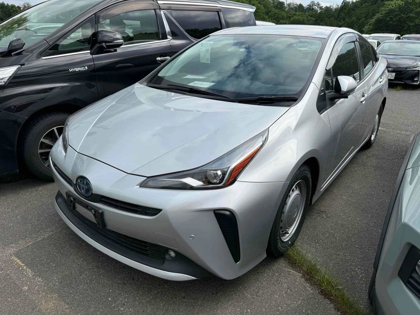 Toyota Prius hybrid hatchback - Front-left exterior showing white pearl paint, LED headlights, and modern grille in parking lot setting