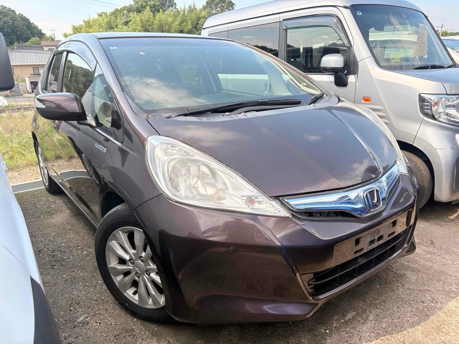 Maroon-burgundy Honda Fit Hybrid compact minivan - front-left 3/4 view in outdoor parking lot with good lighting