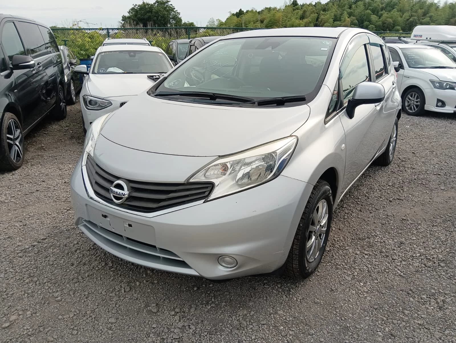 Silver Nissan Note compact hatchback - front-left 3/4 view in outdoor lot showing LED headlights and modern grille design