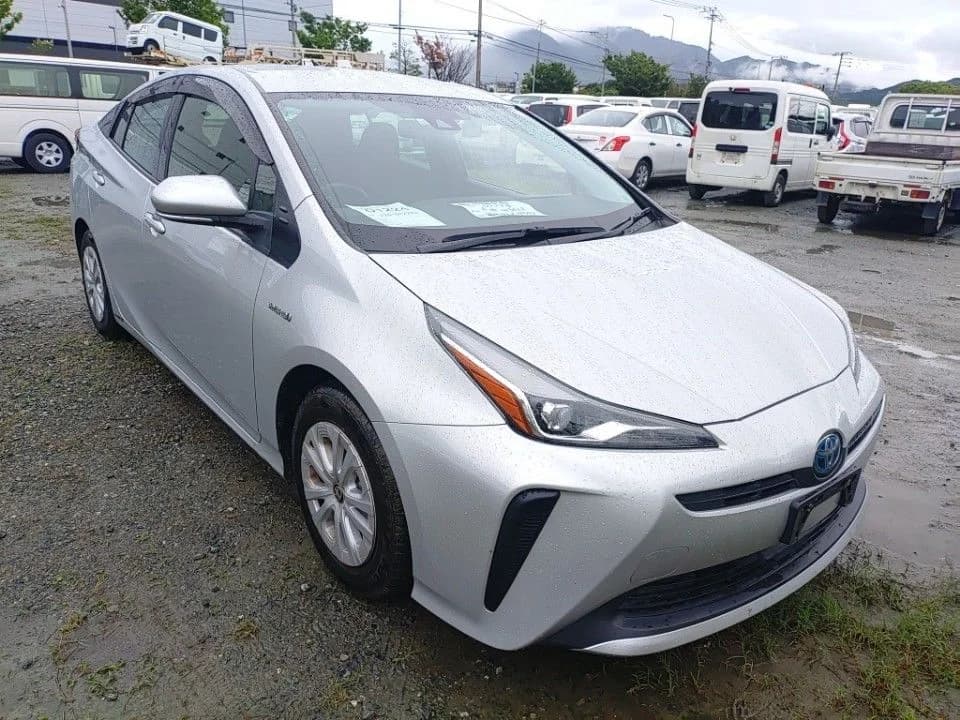 Toyota Prius hybrid sedan - Front-left 3/4 view showing white pearl paint, LED headlights, and modern design at dealership lot with mountains