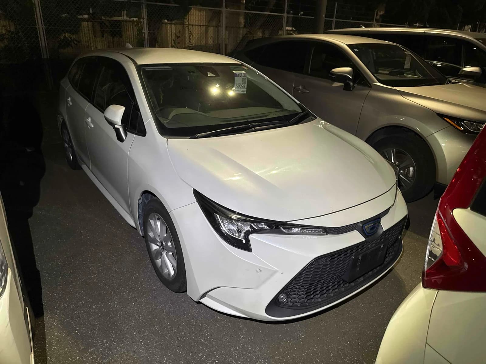 Toyota Corolla hatchback - Front-left 3/4 view showing white pearl paint, LED headlights, and compact modern design at night