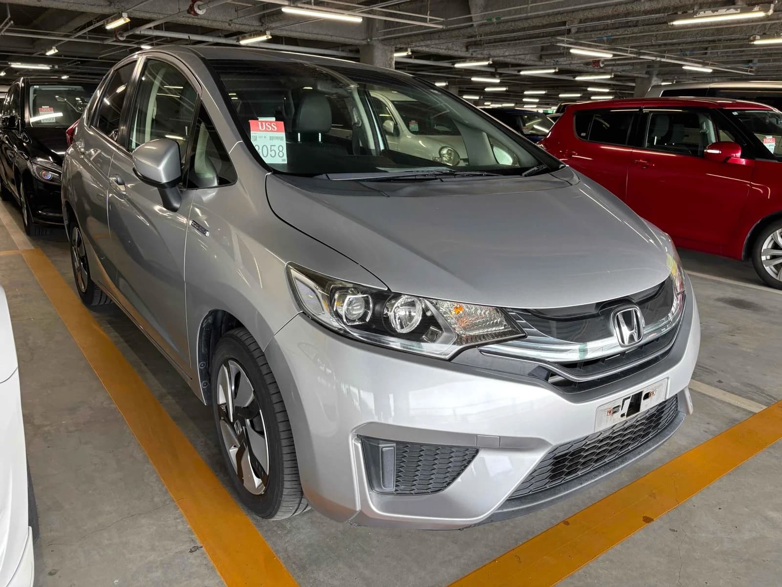 Silver Honda Fit compact hatchback - front-left 3/4 view in parking structure showing the modern grille, LED headlights, and hood