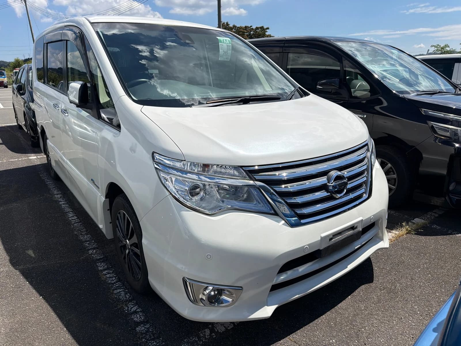 White Nissan S-Cabin van - front-left 3/4 view showing the distinctive large chrome grille and LED headlights in natural daylight
