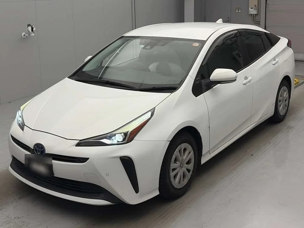 Toyota Prius hybrid sedan - Front-left 3/4 view showing white pearl paint, LED headlights, and modern design in warehouse