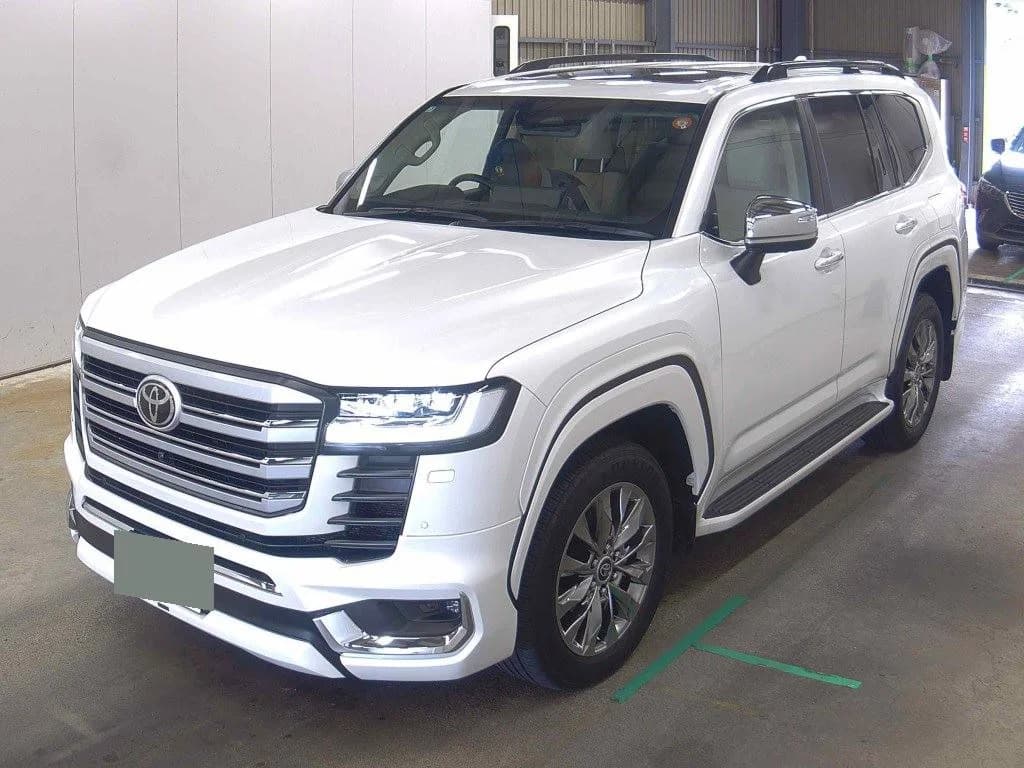 White Toyota Land Cruiser ZX SUV front-left three-quarter view in indoor garage with roof rails, chrome grille, and LED headlights
