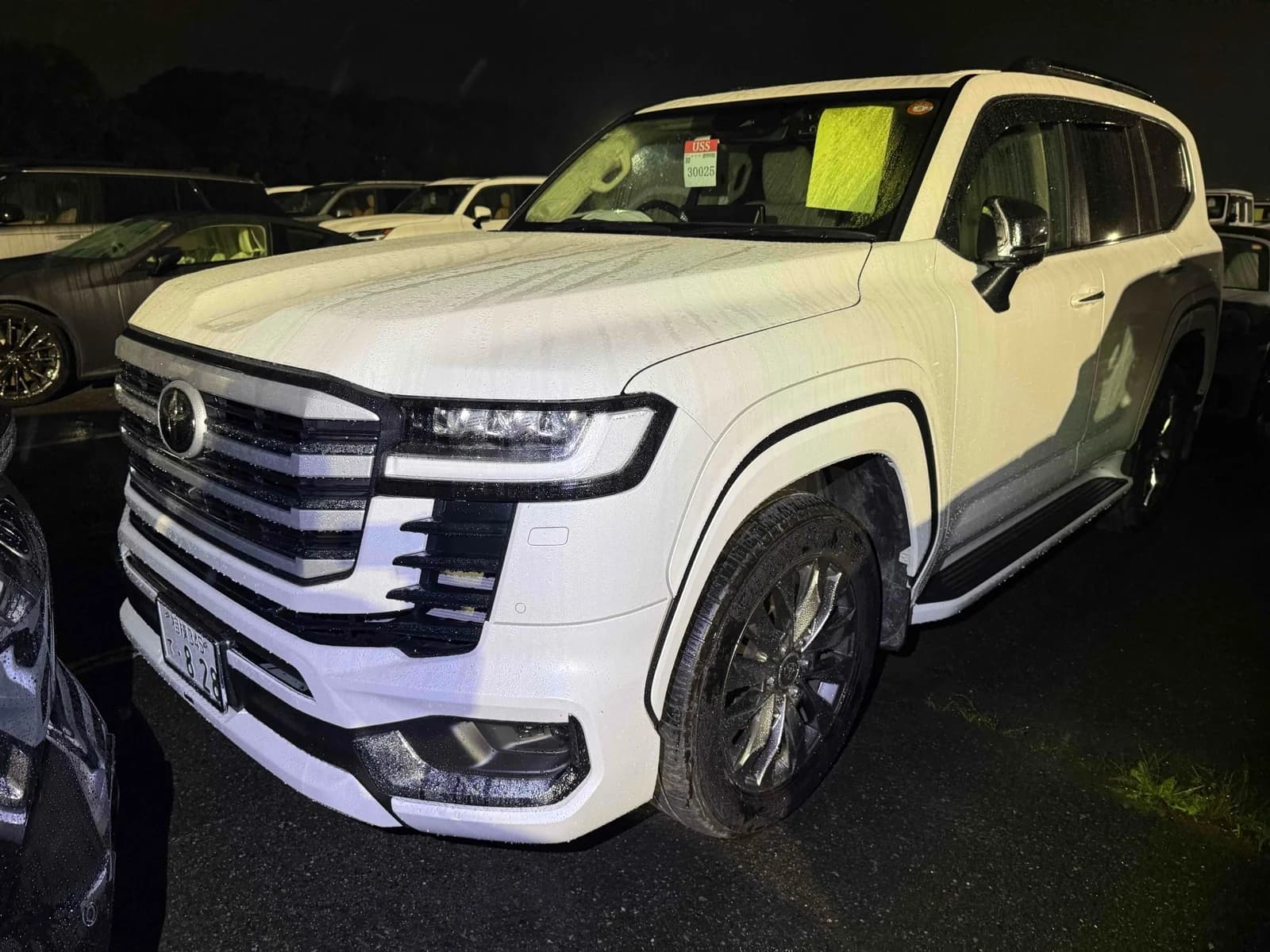 White Toyota Land Cruiser SUV front-left three-quarter night view at auction lot with wet paint and black alloy wheels