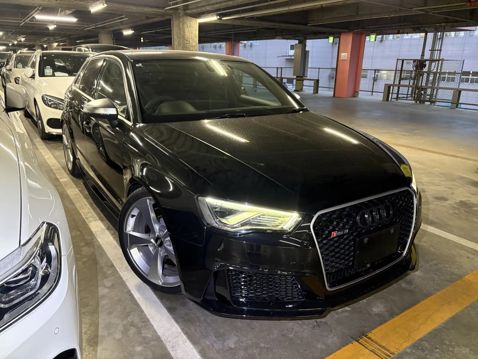 Black Audi RS3 Sportback front-right three-quarter view in indoor parking garage with honeycomb grille and LED headlights