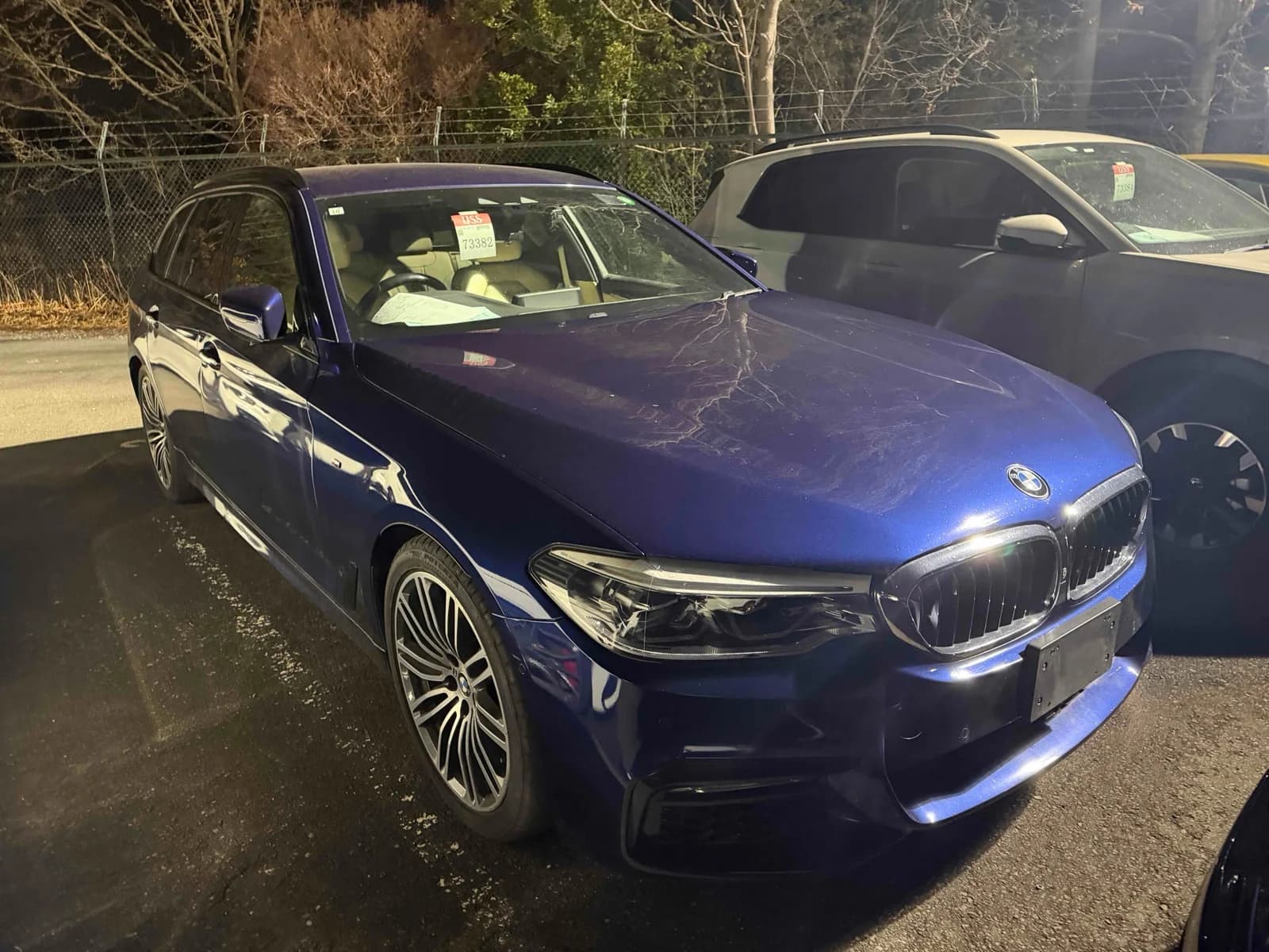 Blue BMW 5 Series Touring wagon front-right three-quarter night view at outdoor auction lot with M Sport bumper