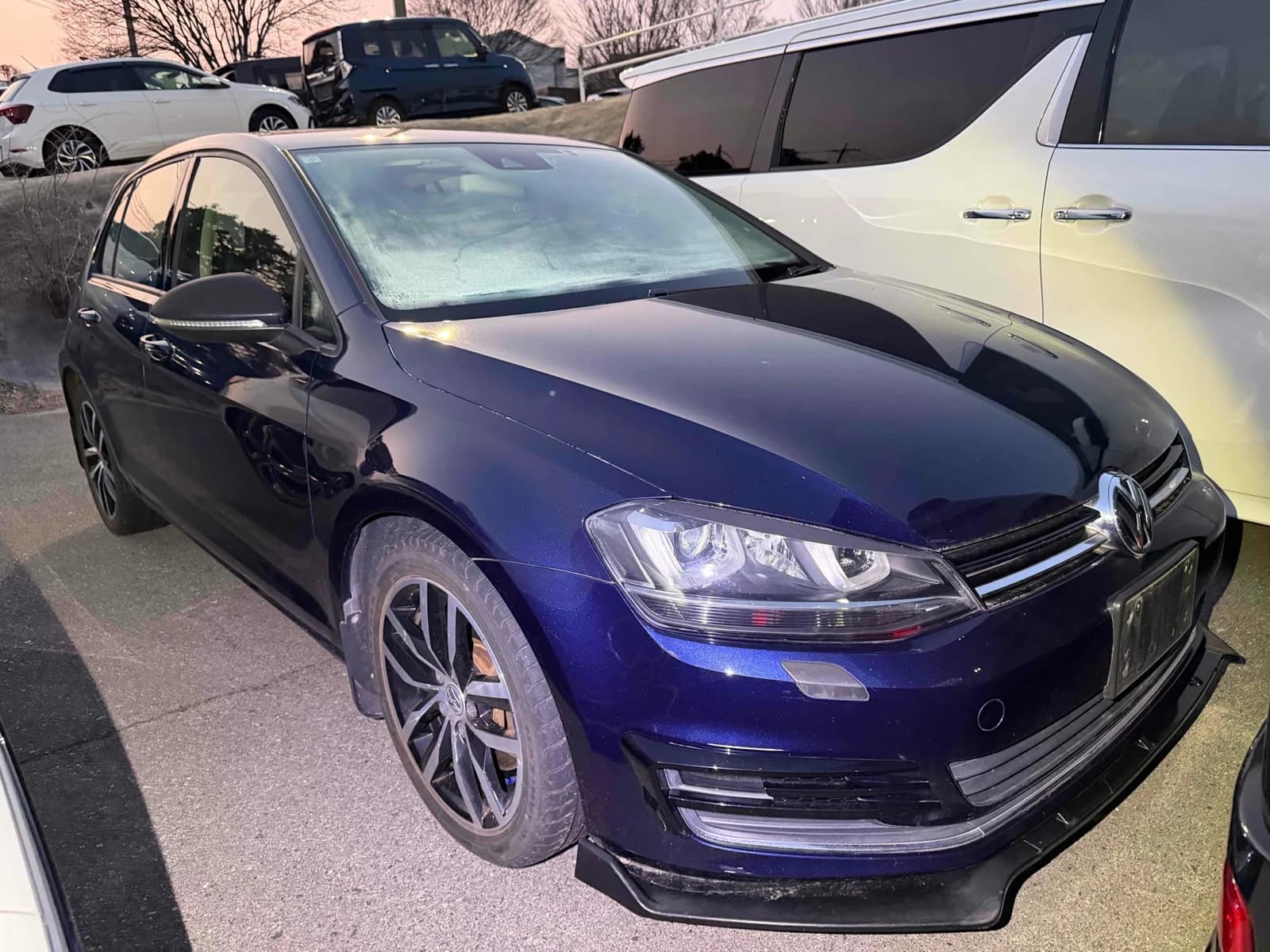 Dark blue Volkswagen Golf hatchback front-right three-quarter view at dusk in outdoor auction lot with black R-Line front splitter