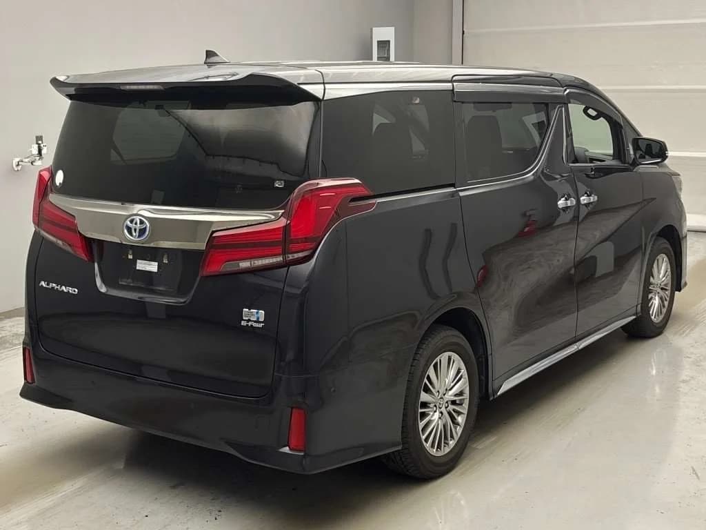 Black Toyota Alphard minivan rear three-quarter view in warehouse