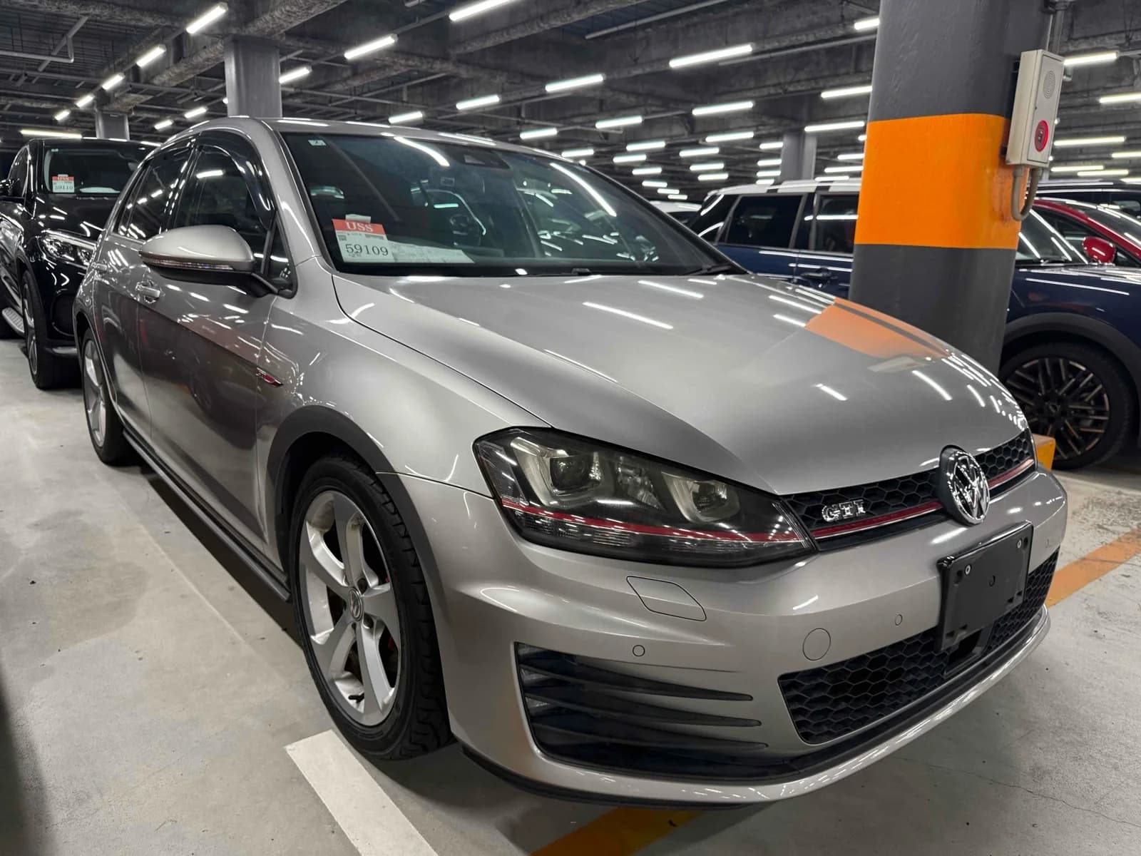 Silver Volkswagen Golf GTI hatchback front-right three-quarter view in indoor parking garage with GTI badge and red grille stripe