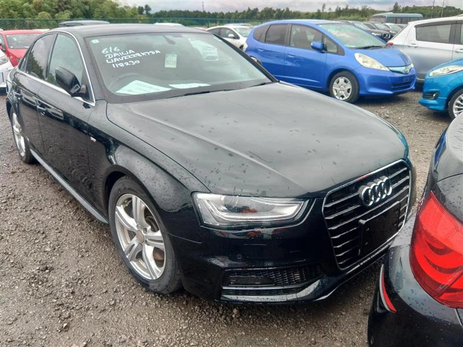 Audi A4 S-Line sedan - Front-right exterior view in an auction lot with black paint, chrome single-frame grille, and multi-spoke alloy wheels