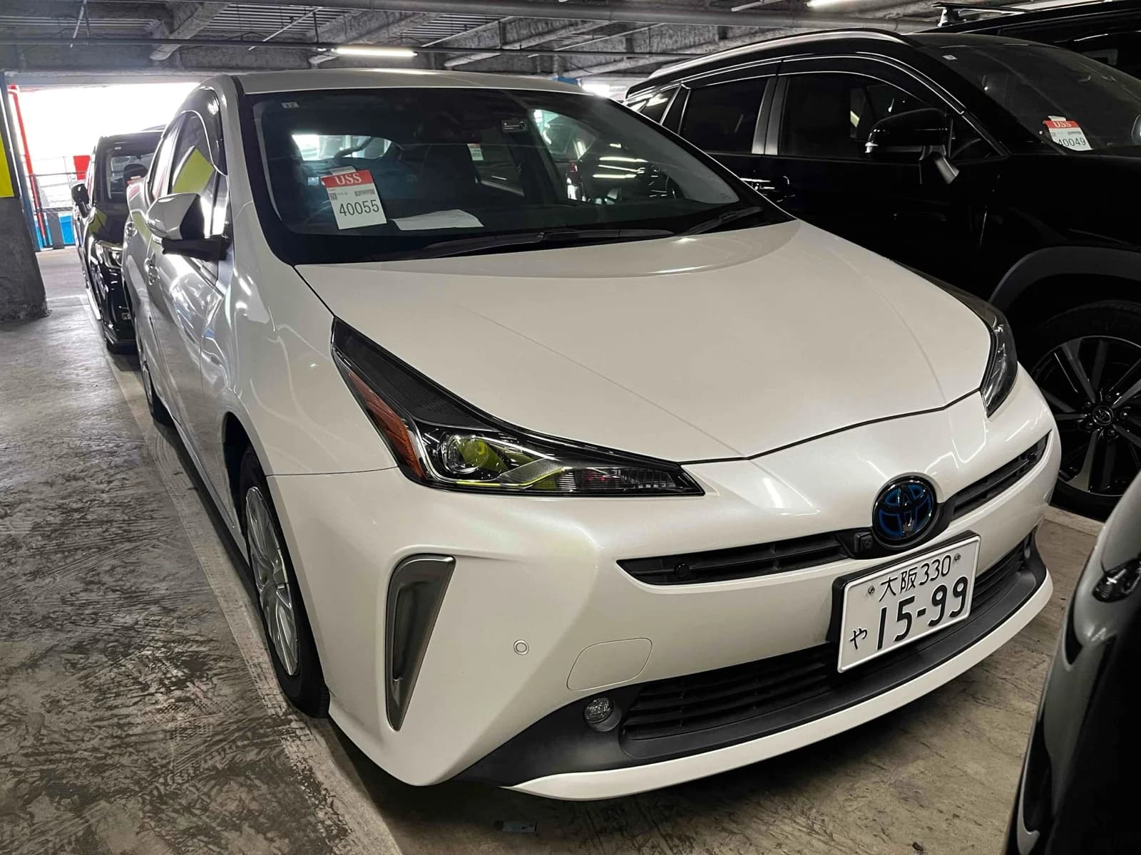 Toyota Prius hybrid hatchback - Front-right exterior view in an indoor parking garage with white pearl paint and Toyota emblem
