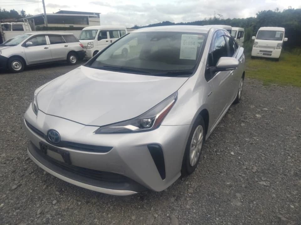 Toyota Prius hybrid hatchback - Front-right exterior view in an outdoor gravel lot with silver paint and Toyota emblem