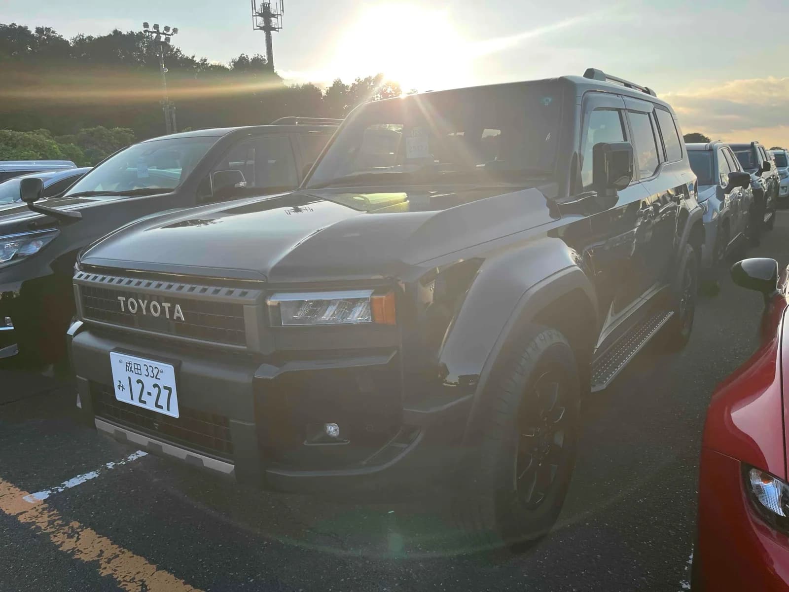 Toyota Land Cruiser 250 SUV - Front-left exterior view at sunset in gray-green paint with matte black hood, LED headlights, and black steel wheels