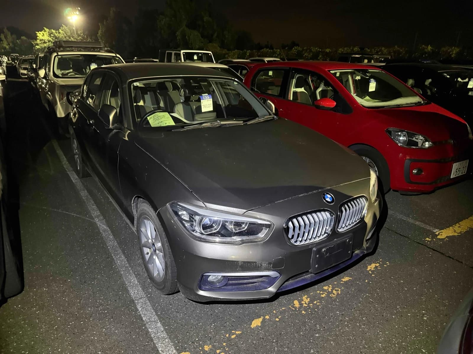 BMW 1 Series hatchback - Front-right exterior view at night in an auction lot with matte gray paint and alloy wheels