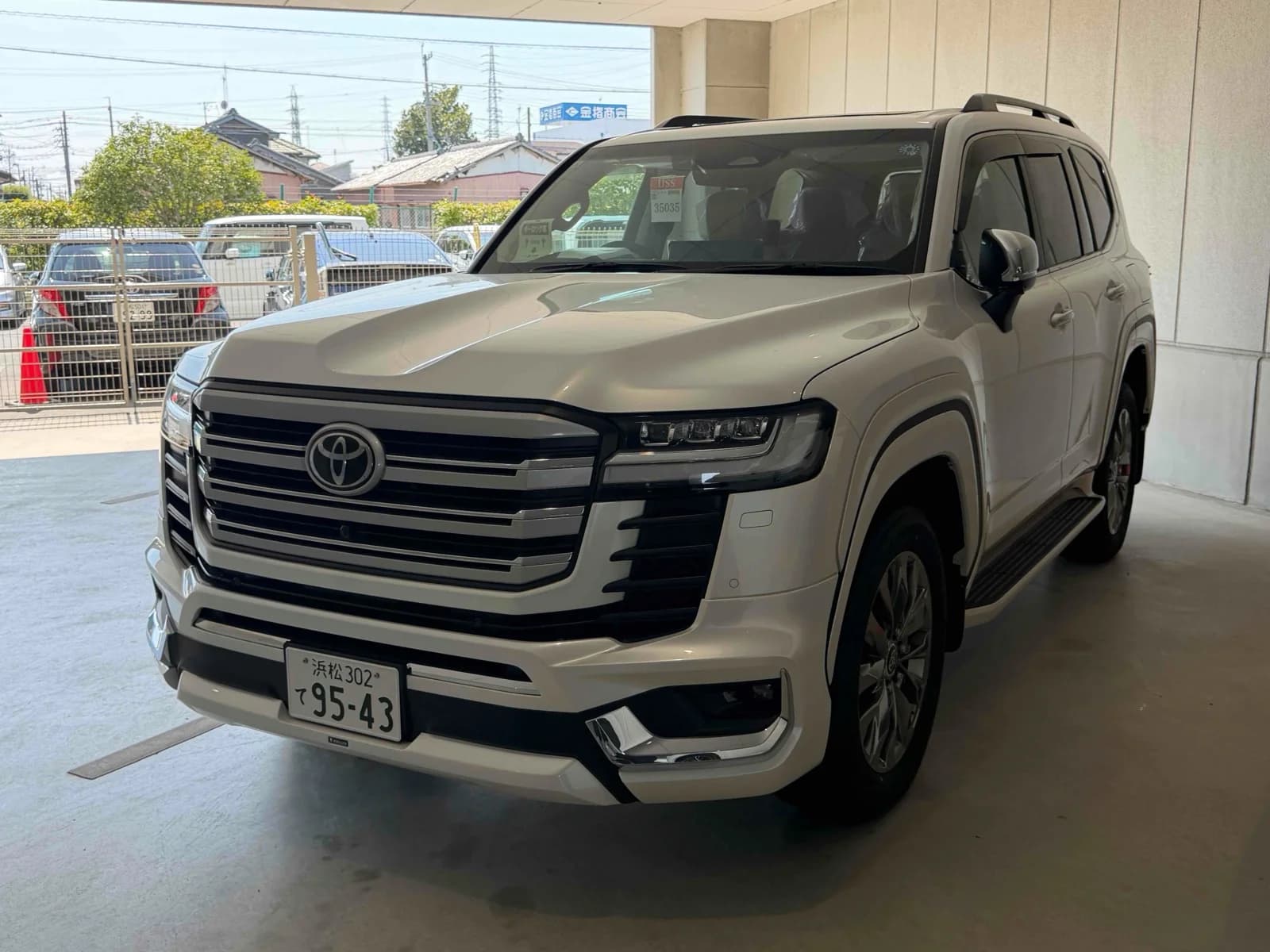 Toyota Land Cruiser 300 ZX SUV - Front-right exterior view in a covered inspection bay with white pearl paint, LED headlights, and chrome grille