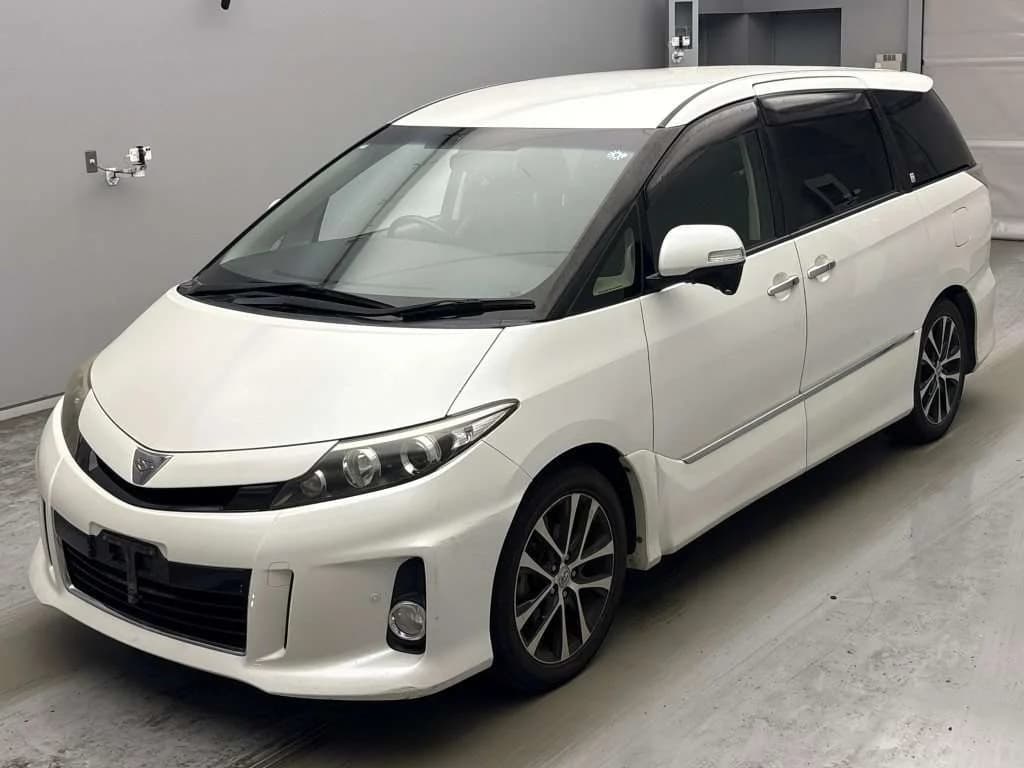 Toyota Estima Aeras minivan - Front-left exterior view in a photo studio with pearl white paint, black roof rails, and dark alloy wheels