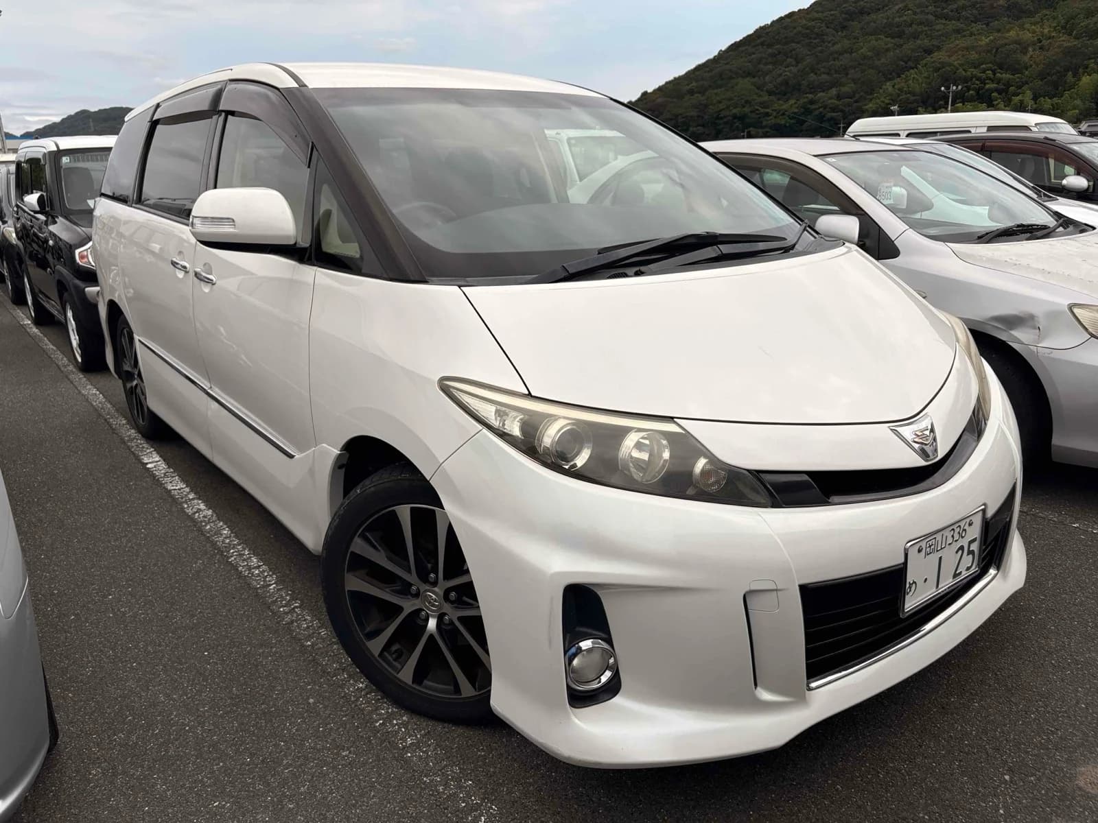 Toyota Estima minivan - Front-right exterior view with white paint, dark tinted windows, LED headlights, and black alloy wheels