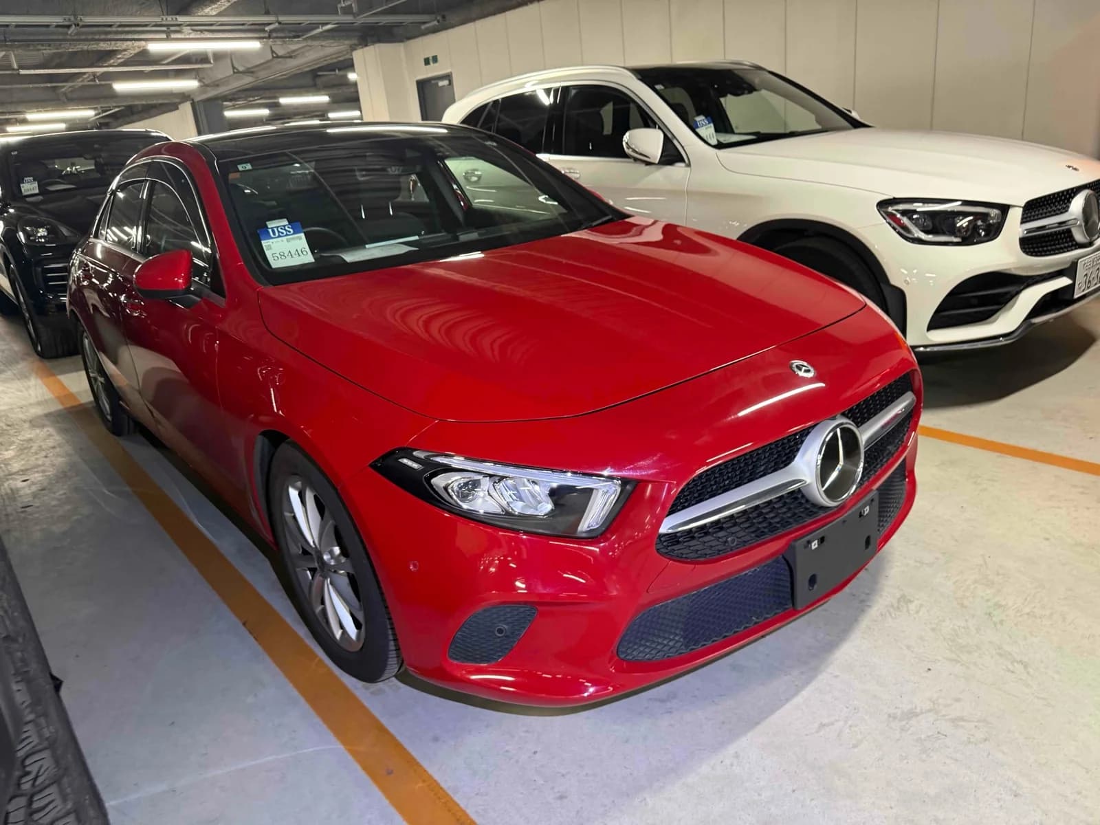 Mercedes-Benz A-Class sedan - Front-right exterior view in a covered inspection bay with red paint, LED headlights, and chrome grille