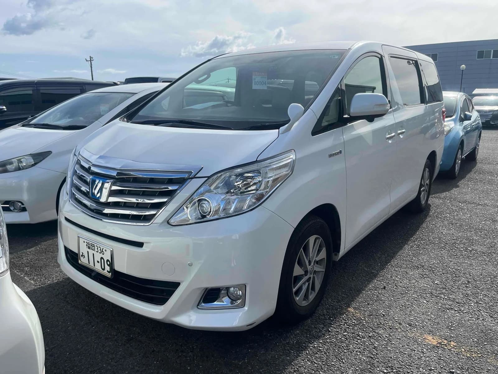 Toyota Alphard Hybrid minivan - Front-right exterior view with pearl white paint, chrome grille, projector headlights, and alloy wheels