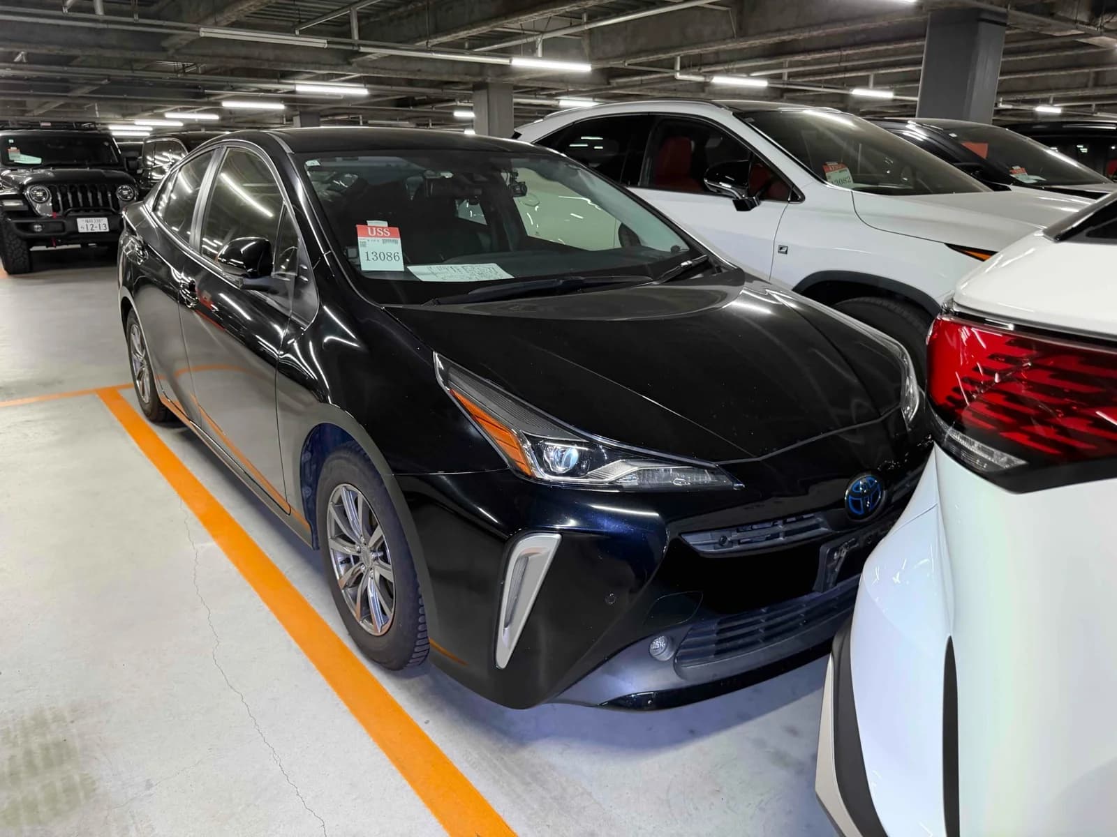 Toyota Prius hatchback - Front-left exterior view with black paint, LED headlights, and USS auction tag on windshield in an indoor lot
