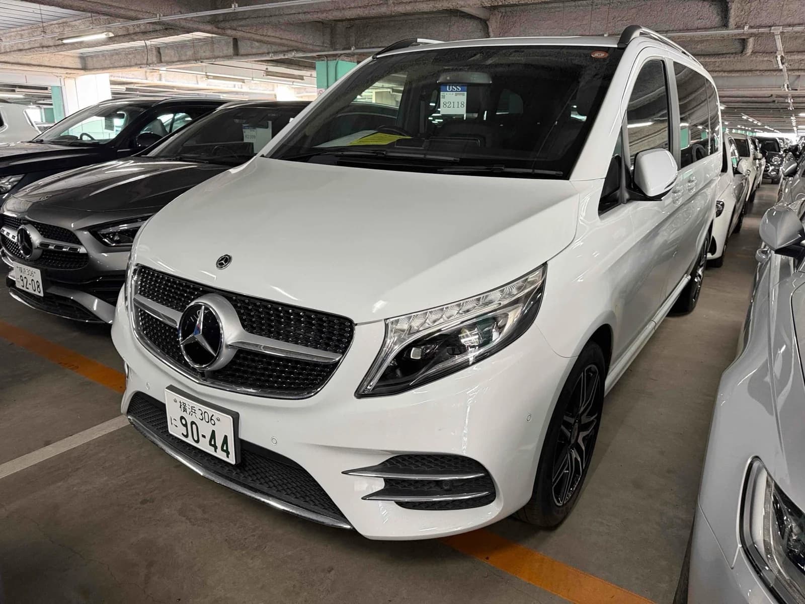 Mercedes-Benz V-Class V220d AMG Line minivan - Front-left three-quarter view in white with diamond-pattern grille, LED headlights, roof rails and black AMG alloy wheels