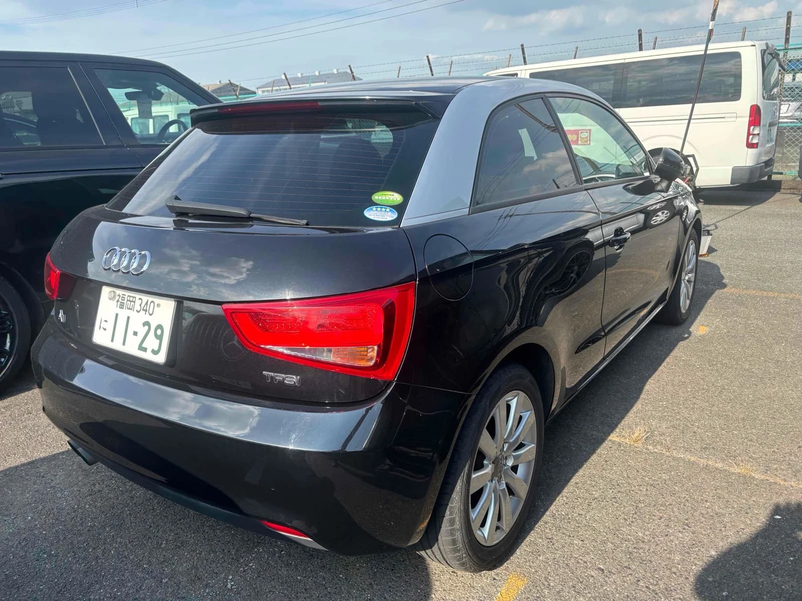Audi A1 TFSI three-door hatchback - Rear-right three-quarter view in black with grey contrast roof, roof spoiler, red taillights and silver ten-spoke alloy wheels