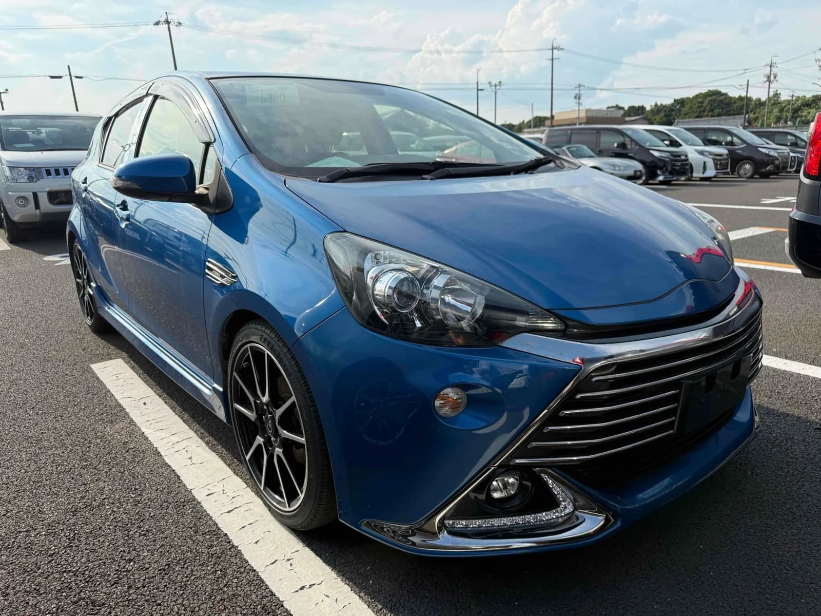 2015 Toyota Aqua G G's hybrid in metallic blue - front-right 3/4 view with chrome-slat G's grille, LED daytime running lights, and 17-inch alloy wheels