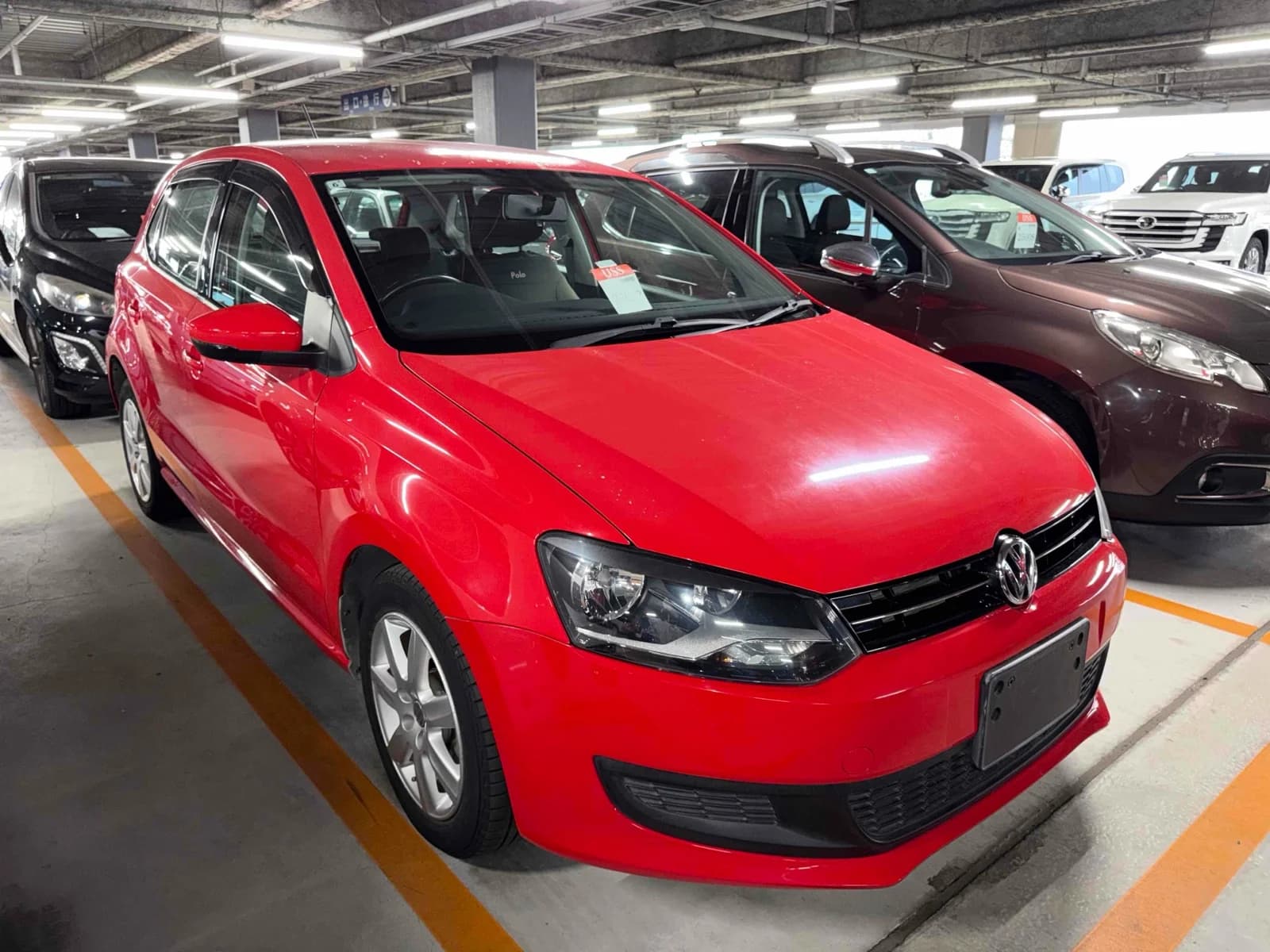 2013 Volkswagen Polo TSI Comfortline BlueMotion in red - front-right 3/4 view with halogen headlights, chrome grille, window visors, and 15-inch alloy wheels