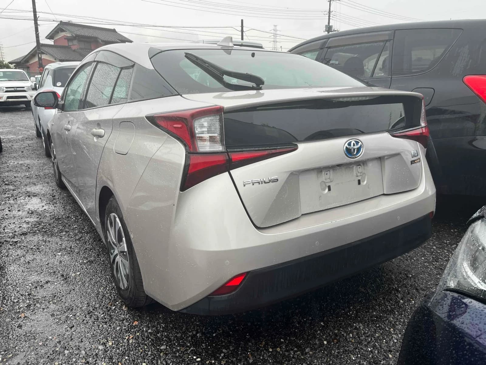 2019 Toyota Prius A hybrid in champagne silver - rear-left 3/4 view with sharp L-shaped LED tail lights, blue hybrid Toyota badge, PRIUS lettering, and rear wiper